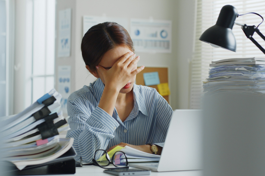 burned out emerging leader with hand on head surrounded by mounds of paperwork on desk.