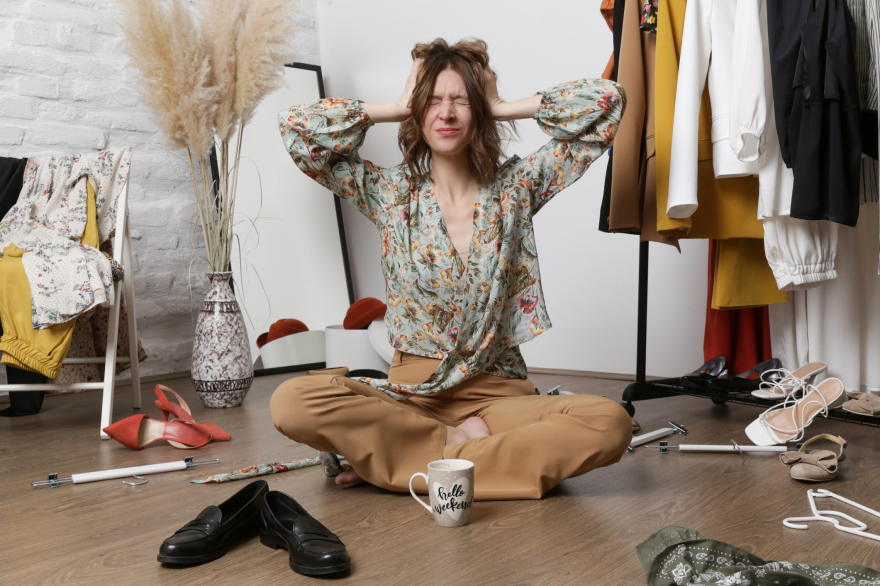 Frustrated woman sitting by a clothing rack—overwhelmed by what to wear before working with Kim Peterson’s styling process.