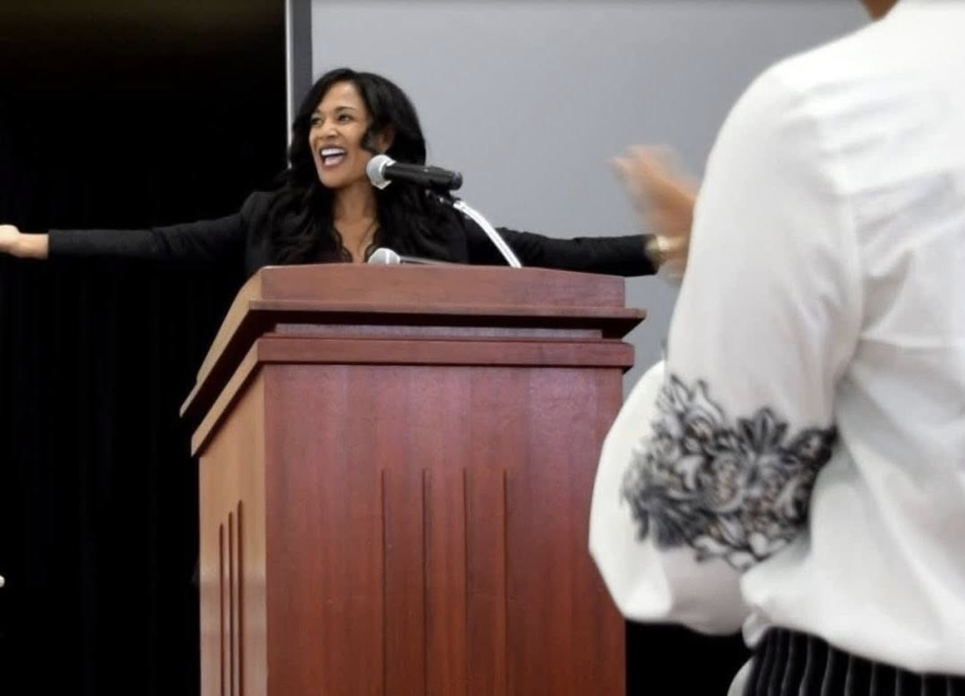 Kim Peterson speaking on stage with open arms as a young girl stands and claps — symbolizing empowerment, courage, and belonging through the Fear to Freedom to R.I.S.E. program for girls and women.