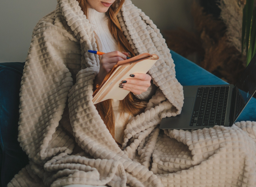 Woman journaling with a blanket and laptop — reflecting on goals for self-leadership and healing. Woman journaling—self-reflection for healing.