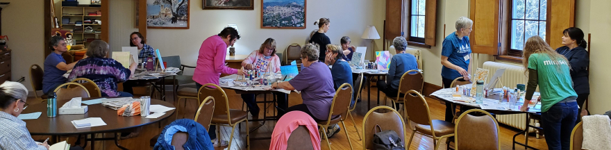 people gathered around tables, painting on canvasses