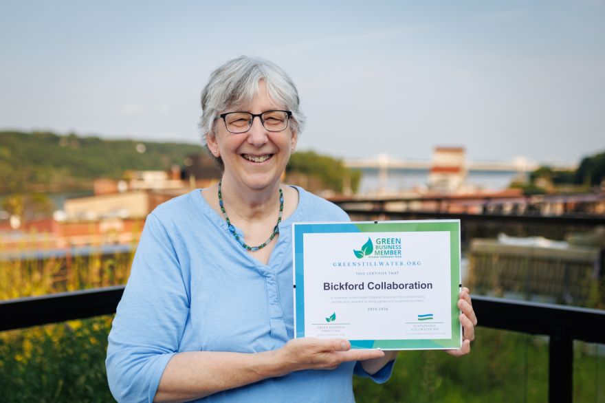 Barb Bickford holding a Green Business certificate, with the city of Stillwater in the background