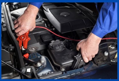 A mechanic is jumpstarting a car with booster cables