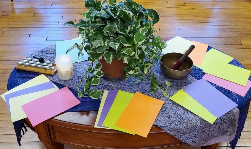 A low table with a potted plant, candle, brass bowl and colored papers on it