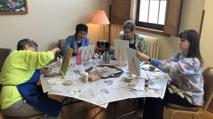A group of women, painting at a table covered in newsprint