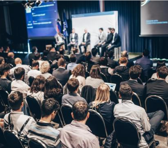 A panel of speakers on a stage facing many rows of listeners