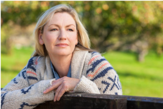 A middle aged woman in a sweater, thoughtfully looking off into the distance