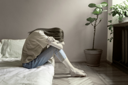 Woman sitting on mattress with head in arms
